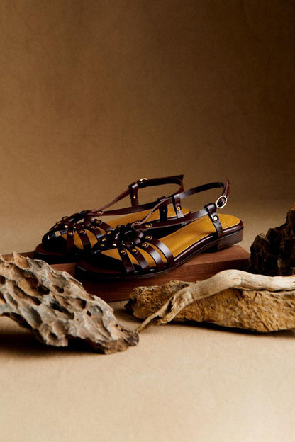 Sandalias color tierra con tiras entrelazadas y tachuelas metálicas doradas, plana
