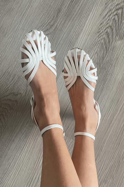 Sandalias blancas con tiras cruzadas y pulsera ajustable; suela plana.