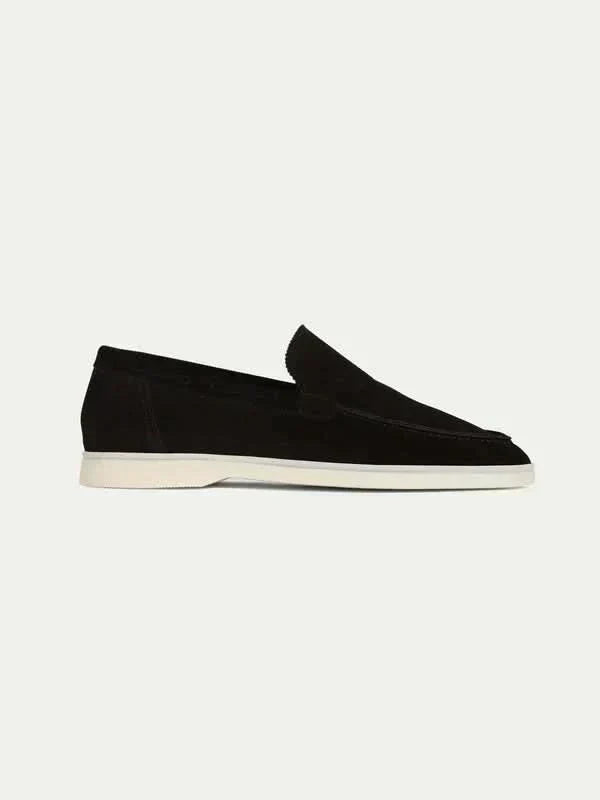 Mocasín de ante negro con suela blanca, estilo mocasín y lengüeta integrada.