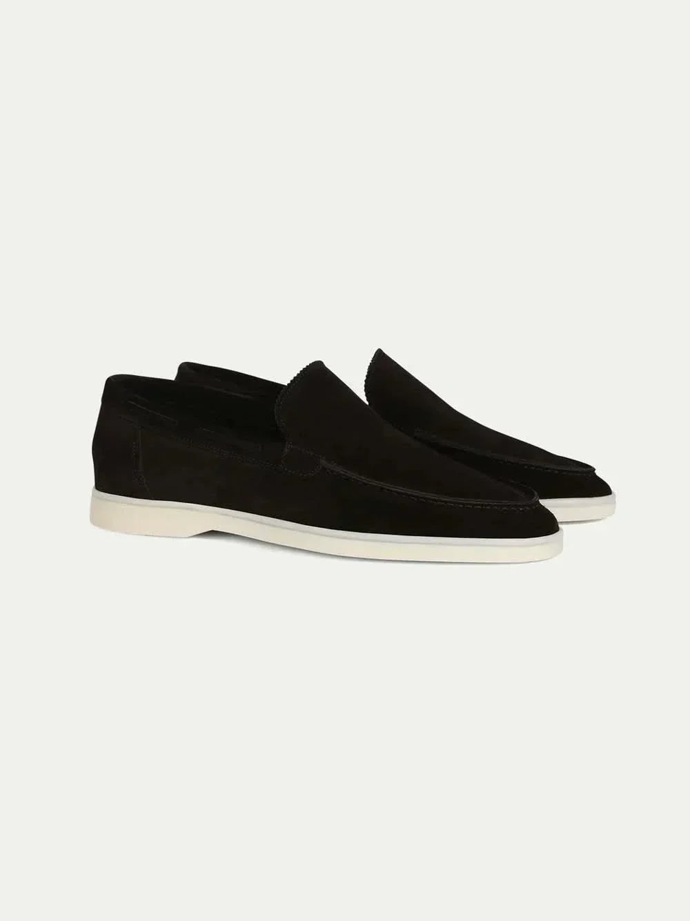 Mocasines de ante color negro, estilo slip-on, suela blanca y costuras frontales.