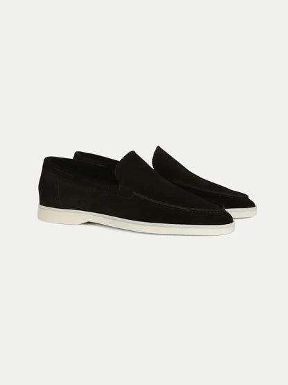 Mocasines de ante color negro, estilo slip-on, suela blanca y costuras frontales.