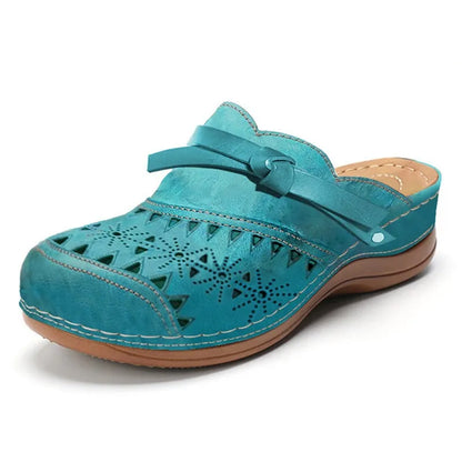 Zueco ortopédico verde azulado con perforaciones, tira ajustable y suela de cuña marrón
