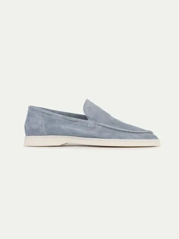 Mocasín de ante azul grisáceo con suela blanca, sin cordones y costura lateral.