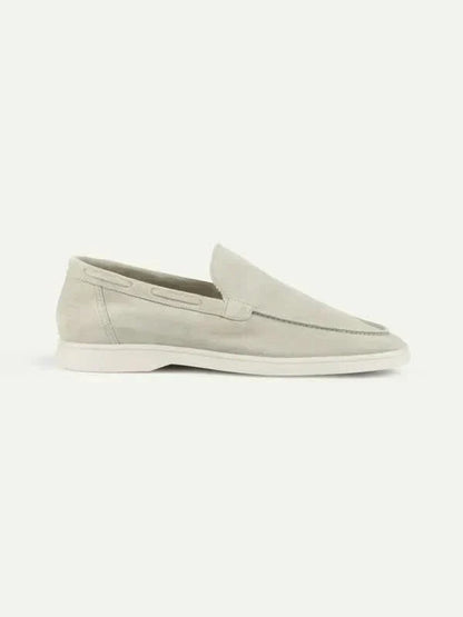 Mocasín de ante beige claro con suela blanca, sin cordones y costura frontal.