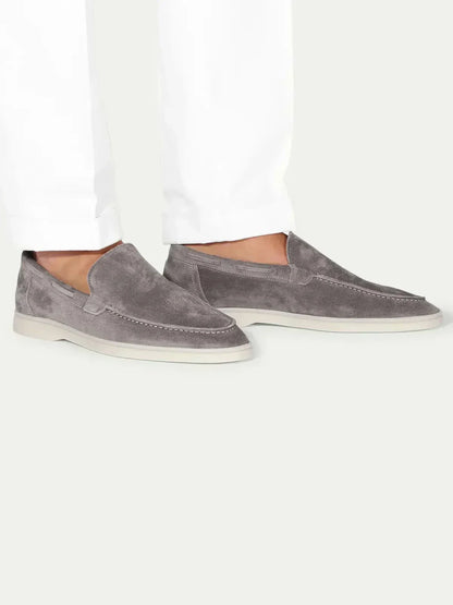 Mocasines de ante gris, slip-on, con suela blanca y plantilla visible.
