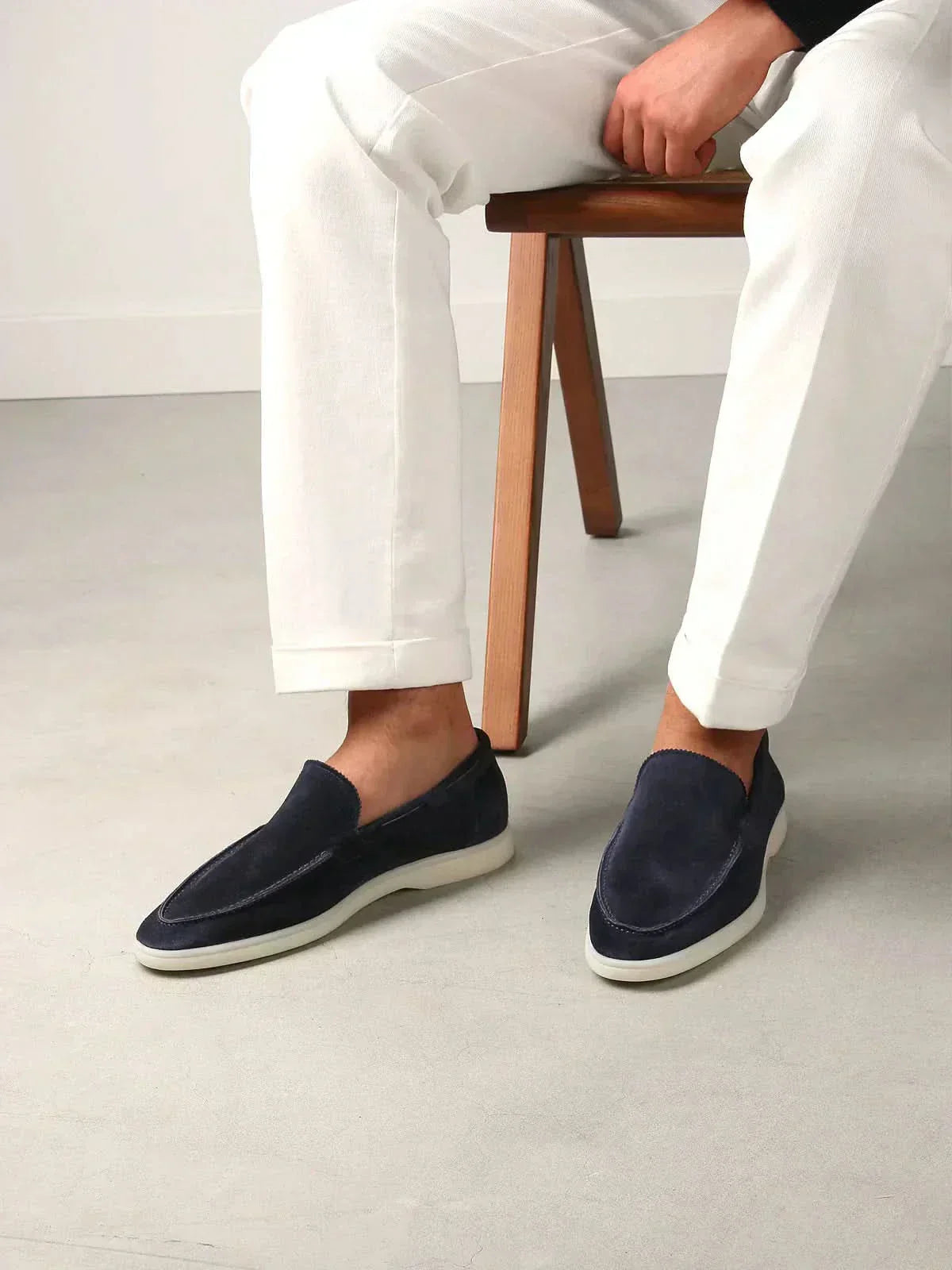 Mocasines de ante azul marino con suela blanca, con pantalón blanco visible.