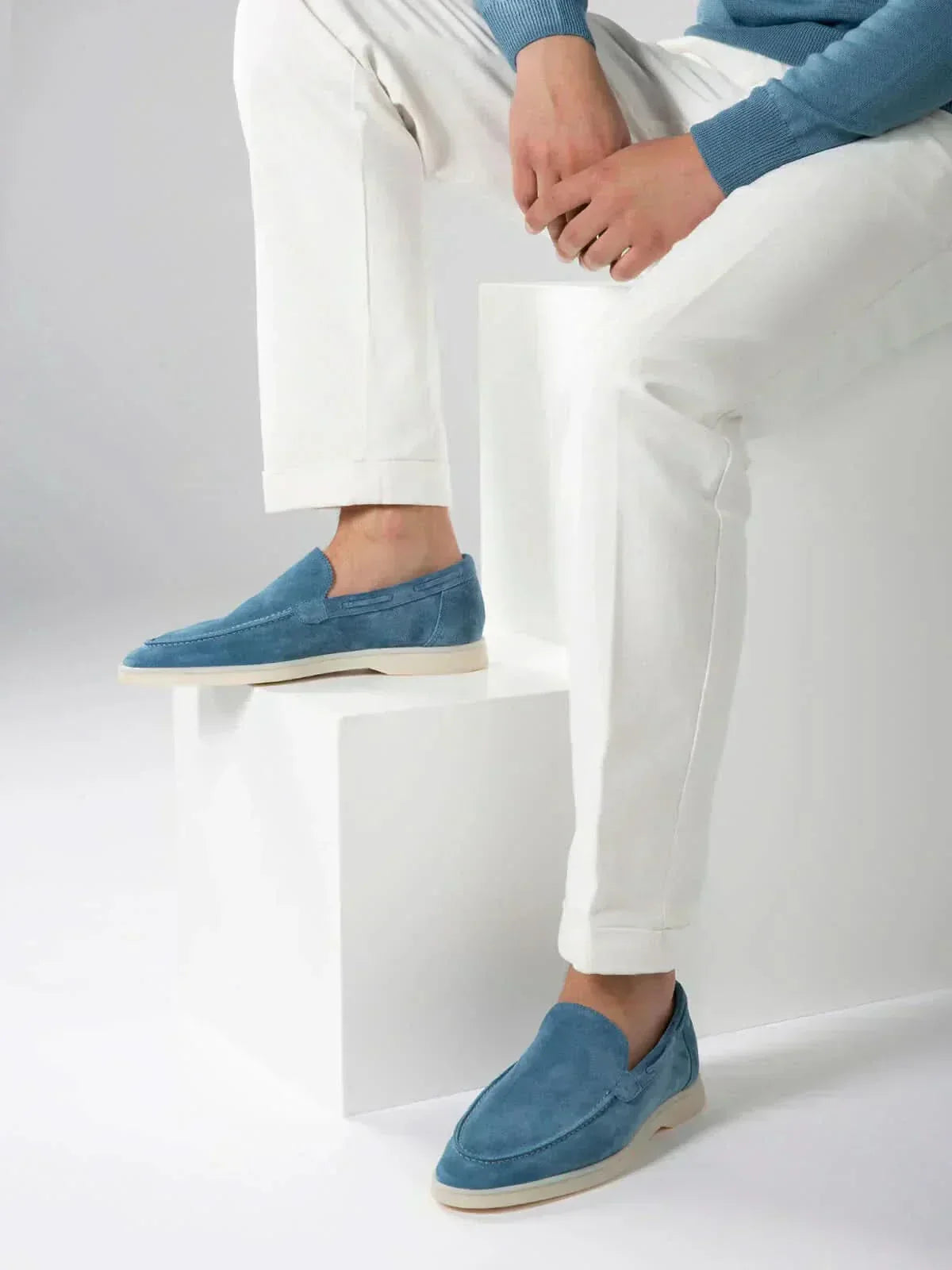 Mocasines de ante azul, estilo slip-on, con suela clara y pantalón blanco/jeans.