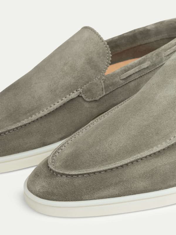 Mocasines de ante gris claro, slip-on, con suela blanca y costuras.