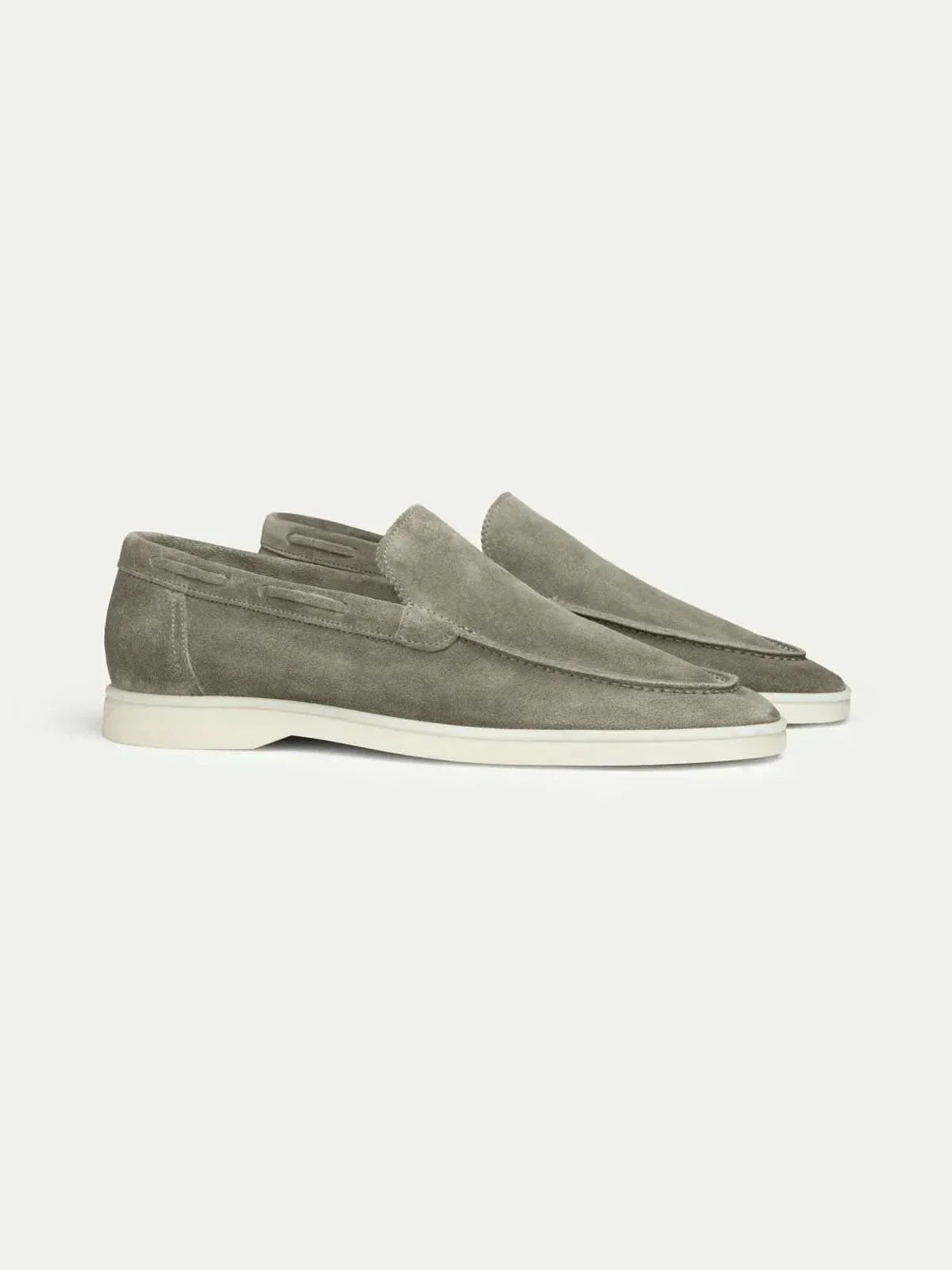 Mocasines de ante color gris topo, estilo slip-on, suela blanca y costuras.